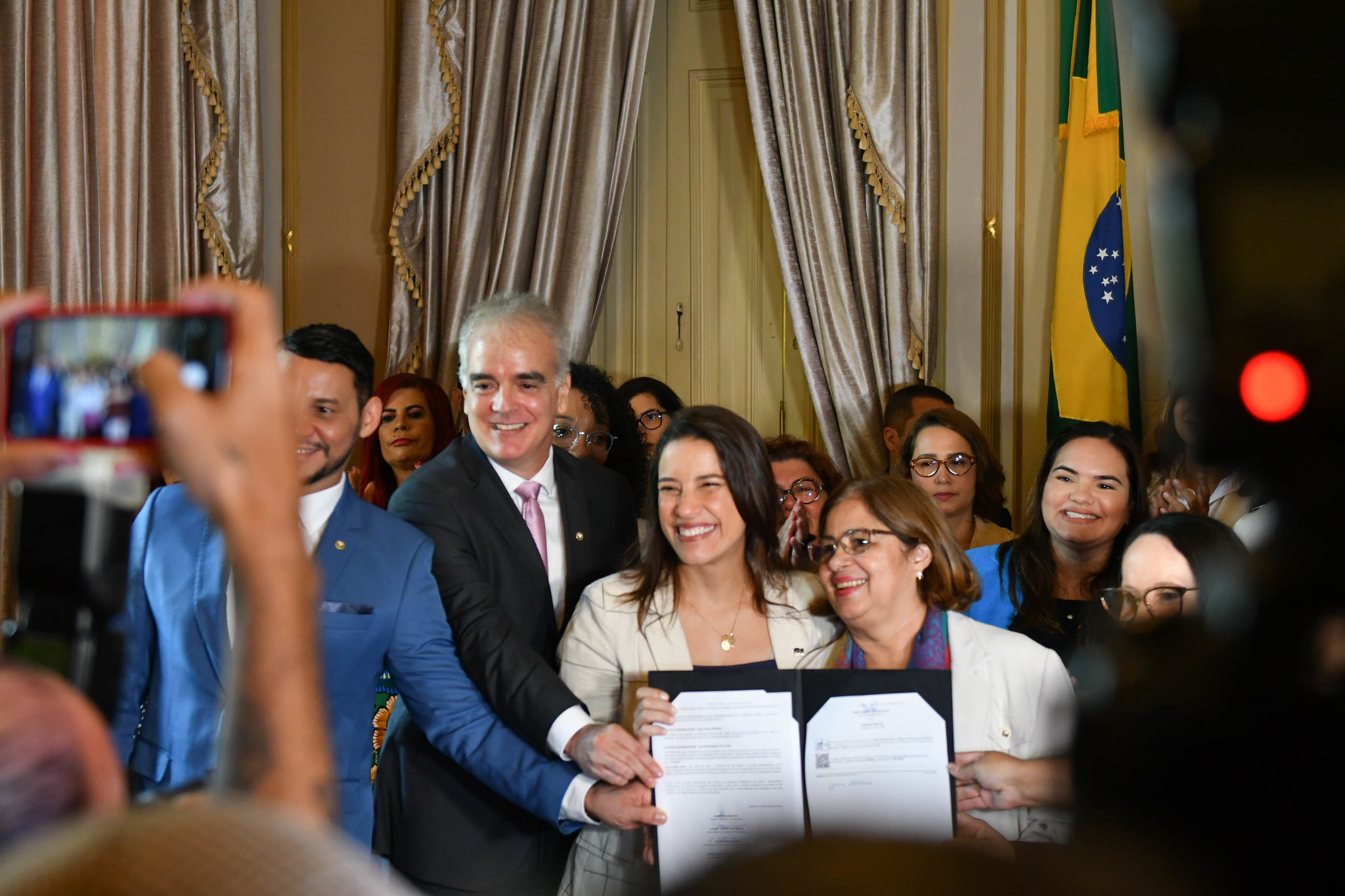 Fotografia do PGJ segurando o documento assinado junto à governadora e ministra