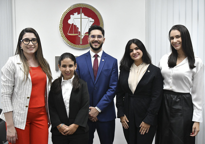 Foto mostra quatro mulheres e um homem, de pé. Eles estão em frente a uma parede branca com o brasão do MPPE ao fundo.