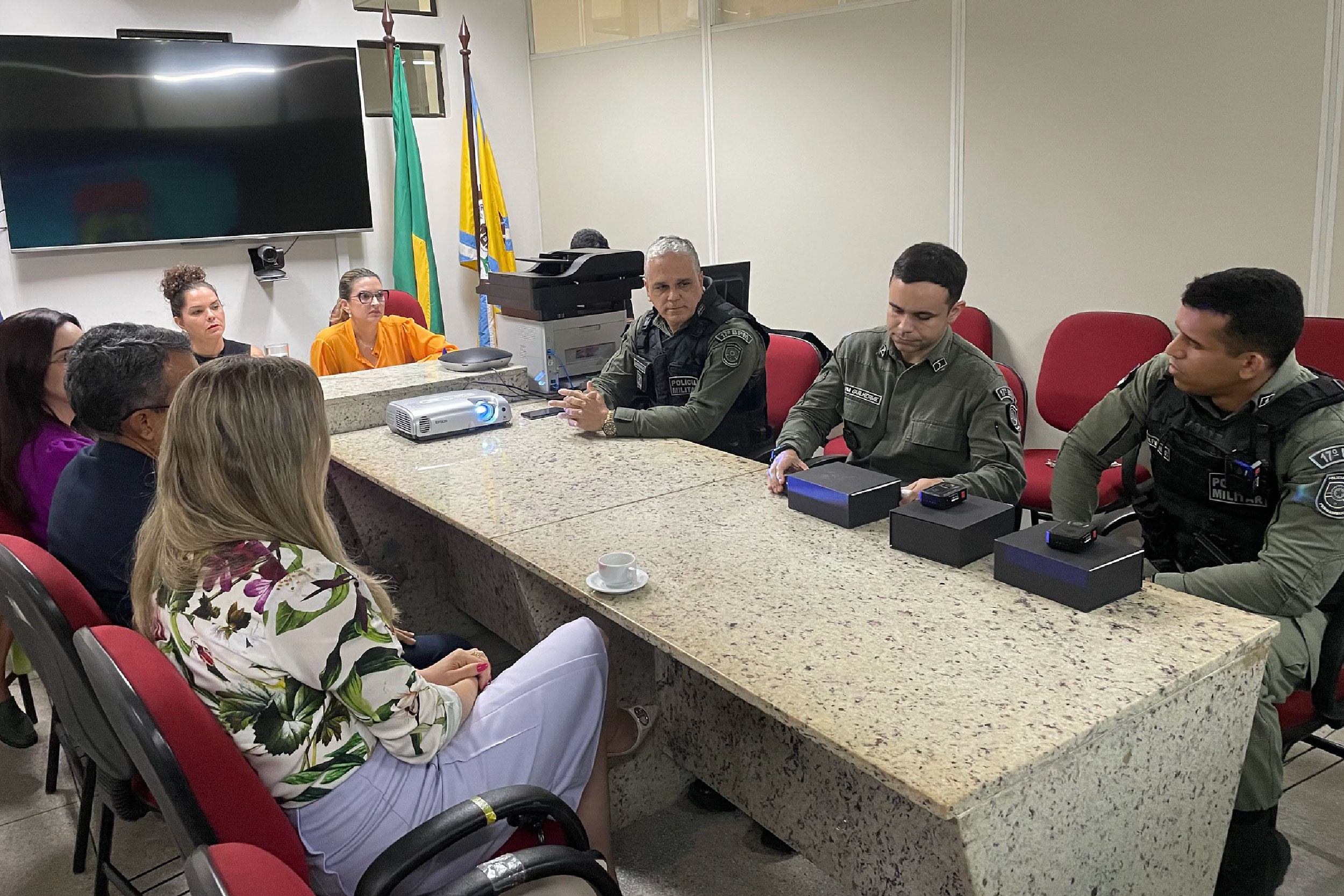 Fotografia de pessoas sentadas em volta de mesa de reunião com aparelhos eletrônicos 