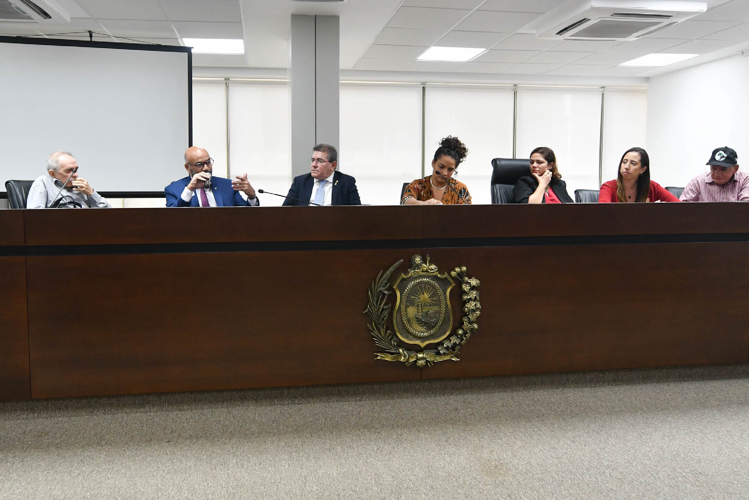 Fotografia de pessoas que participaram da reunião sentadas atrás da bancada 